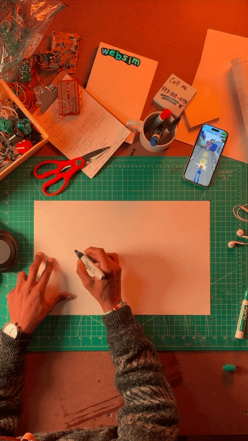 Animated view of a desk setup with paper, tools, and a phone beside a blank drawing canvas
